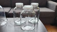 Three large clear glass jars with spring clamp lids on a table in front of a couch.