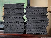 Two stacks of black egg crate style acoustic foam tiles shown, approximately 23 tiles in each stack for a total of 46 pieces. The tiles have a textured surface designed to absorb sound waves.