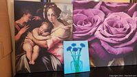 Three large art prints displayed including classical painting of woman and baby, large purple rose close-ups, and smaller floral blue print centered