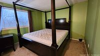 Canopy bed frame assembled with posts and rails, dark wood finish, nightstand visible beside bed.