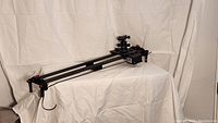 Motorized camera slider laid horizontally on white fabric background, showing dual rails, sliding carriage, motor housing, and power cable
