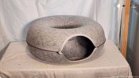 Gray felt circular cat bed zipped closed with a visible entrance opening.