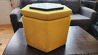 Front angle showing the hexagonal foot stool with yellow upholstery and removable lid with black tray inset. Upholstery is worn and damaged on edges.