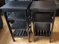 Two black Ikea shelves side by side on wooden floor, one showing lifted adjustable shelf to demonstrate functionality.