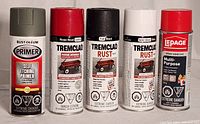 Five spray cans photographed side by side, showing front labels and different colored caps.