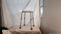 Front view of the adjustable height stool with aluminum legs, round seat, and rubber tips on each leg, set against a white backdrop.