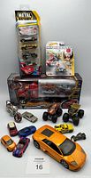 Wide shot of all the toy vehicles including boxed car transporter truck, various diecast cars, motorcycles, monster trucks, large orange sports car model, and Mario Kart Toad figurine.