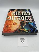 Hardcover book titled 'The Illustrated Encyclopedia of Guitar Heroes' front cover with guitar and guitarist images.