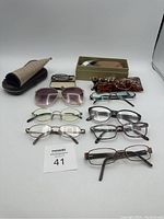 Full lot of seven eyeglasses and three carrying cases on white background.