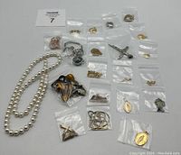 Full lot overview showing white bead necklace, several pendants and chains in small bags arranged on a white surface.