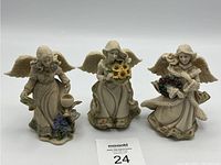 Front view of three porcelain angel figurines dressed in robes and holding flowers, showing detailed painting and wings.