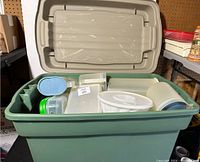Green plastic tote filled with assorted white and translucent Tupperware containers with some lids visible inside the tote.