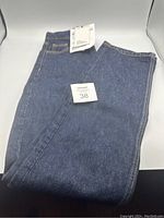 Blue denim jeans folded flat with original size tag attached, showing size 38.