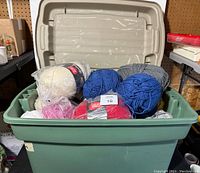 Plastic tote holding mixed yarn skeins in multiple colors and brands, mostly Red Heart Comfort.