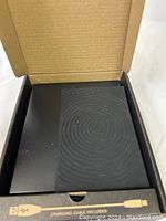 Open box showing Timemore Black Mirror Basic coffee scale with black textured circular pattern weighing surface and packaging with charging cable compartment.