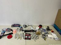 Overview of assorted new construction and tool accessory items on white table, includes safety glasses, clamps, measuring tape, rubber mallet, wiring, and hardware parts.