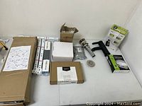 Overview of lot items spread out on table including boxed and loose items such as drawer sliders, cabinet hinges, metal sealing ring, pop-up drain assembly and handle pull.