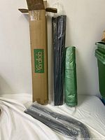 Various parts of the Kardlab greenhouse kit including metal rods and green mesh netting against a white background.