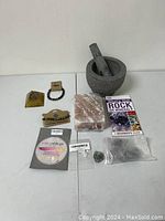 Full view of lot contents including granite mortar and pestle, salt rock slab, bracelets, loose stones, sterling silver earrings, and rock guide book.