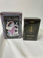 Photo showing the two tarot decks in original sealed packaging: SANIME TAROT by Natasha Velazquez and WYSPELL deck with black and gold celestial design.