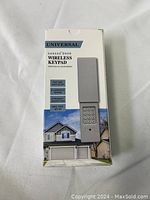 Front view of the box showing the Universal Garage Door Wireless Keypad with features and picture of a house with garage.
