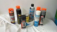 Full view of eight aerosol spray cans and a roll of white tape arranged on a white surface.