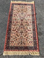 Full view of rectangular 100% wool pile rug with colorful animal and floral patterns and fringe on shorter sides, lying flat on pavement.