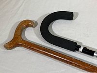 Close-up of the contoured curved wooden cane handle with natural wood finish and black foam hooked handle of the aluminum cane
