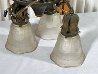 Three frosted glass globes with scalloped edges and heavy embossed floral and linear patterns attached to an aged metal fixture.