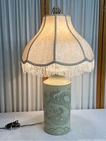 Front view of the ivory ceramic lamp with dragon illustrations and silk shade with fringe trim