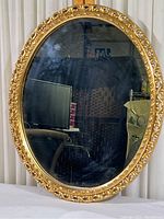 Full view of oval mirror showing gold ornate frame and reflective surface