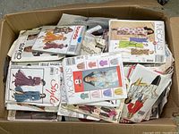 Open cardboard box filled with various vintage women's sewing patterns from multiple brands.