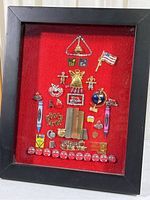 Full view of shadow box frame with teacher pins arranged on red felt background, showing whole item including black wood frame.