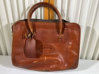Front view of vintage Orvis brown leather briefcase showing embossed logo and attached leather luggage tag.