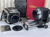 Wide shot of camera body mounted with lens, leather case, bellows unit on rails, lens cap and dark slide laid out