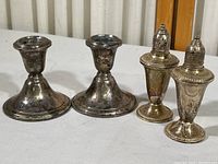 Pair of weighted sterling silver candle holders and salt & pepper shakers on white surface, showing tarnished condition.