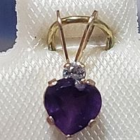 Close-up image of the heart-shaped deep purple amethyst pendant with a small round white sapphire and yellow gold bail on a textured white background.