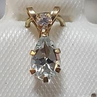 Close-up front view of pear-shaped aquamarine and round white sapphire set in 10K yellow gold pendant.