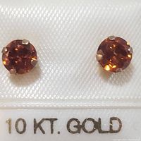 Front view of the paired round Spessartite garnet earrings set in four-prong 10K yellow gold settings on display card.