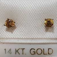 Front view of two round yellow sapphire stud earrings set in 14K yellow gold prong settings on a textured background with '14KT GOLD' text.