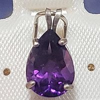 Close-up view of the front face of the purple pear-shaped amethyst gemstone set in a sterling silver pendant with four prongs and a dual-loop bail.