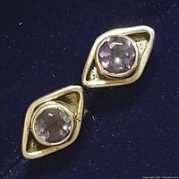 Close-up photo of one sterling silver earring with round faceted amethyst stone set in a geometric diamond-shaped frame on dark blue background.