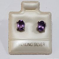 Pair of sterling silver stud earrings with oval purple amethyst gemstones on a white jewelry card stamped 'STERLING SILVER'.