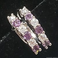 Close-up front view of a pair of sterling silver hoop earrings showing alternating round purple amethyst and clear topaz stones in prong settings.