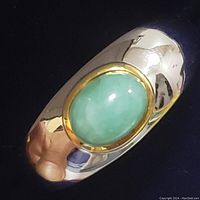 Close-up of sterling silver ring with oval green stone bezel set in gold-tone metal, showing polished band and stone detail.