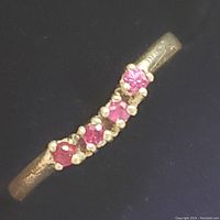 Close-up of sterling silver band with five prong-set round ruby stones in a slight curve.