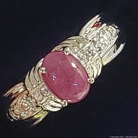 Close-up of sterling silver ring with oval cabochon ruby stone on black background, showing front view with stone and band details.