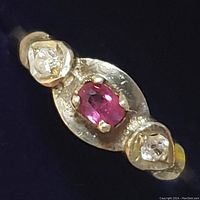 Close-up image of the sterling silver ring with an oval ruby in the center and two clear stones on either side in teardrop-shaped settings, showing the prong details and the band.