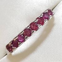Close-up photo of sterling silver ring featuring a row of round faceted ruby stones set in prongs.