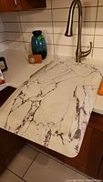 Rubber anti-fatigue kitchen mat with marble pattern placed on kitchen counter near sink.